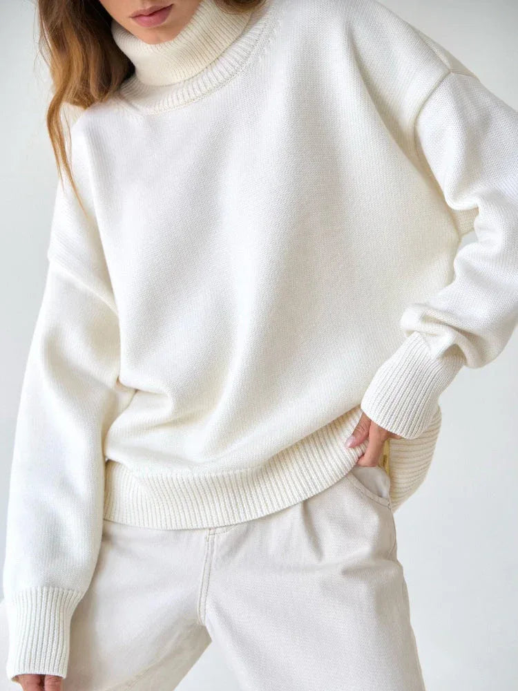 Rear view of a woman wearing an orange oversized turtleneck sweater and dark brown wide-leg trousers.