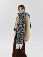 Woman in a beige blazer, brown skirt, and a grey and white leopard print fuzzy scarf with fringe trim, posing with one hand on her hip.