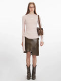 Woman wearing a light pink long-sleeve ruched top with a tie detail and a brown leather skirt