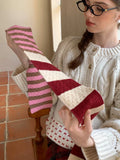 Close-up of a woman holding a striped scarf with alternating burgundy, cream, and pink stripes.