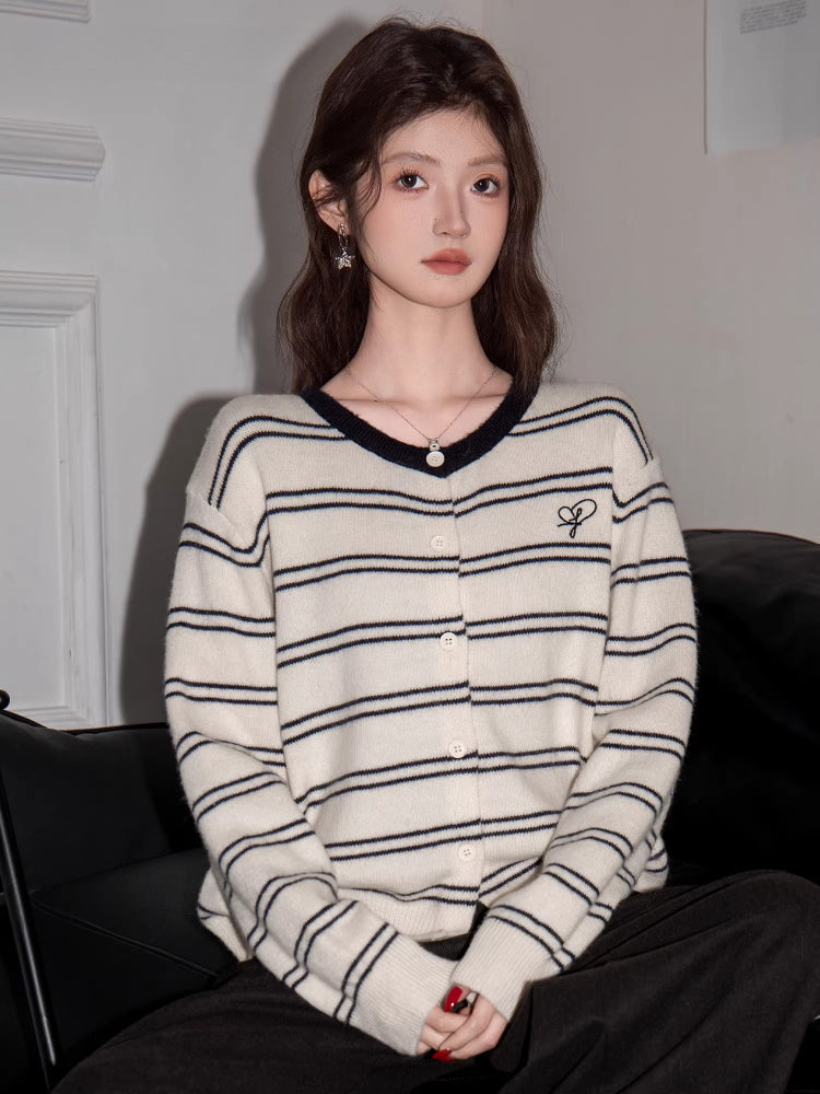 Woman seated, wearing a striped knit cardigan with a V-neck and subtle embroidered logo.