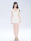 Full body shot of a woman in a white jacquard mini dress with ruffled sleeves and an asymmetrical hem.