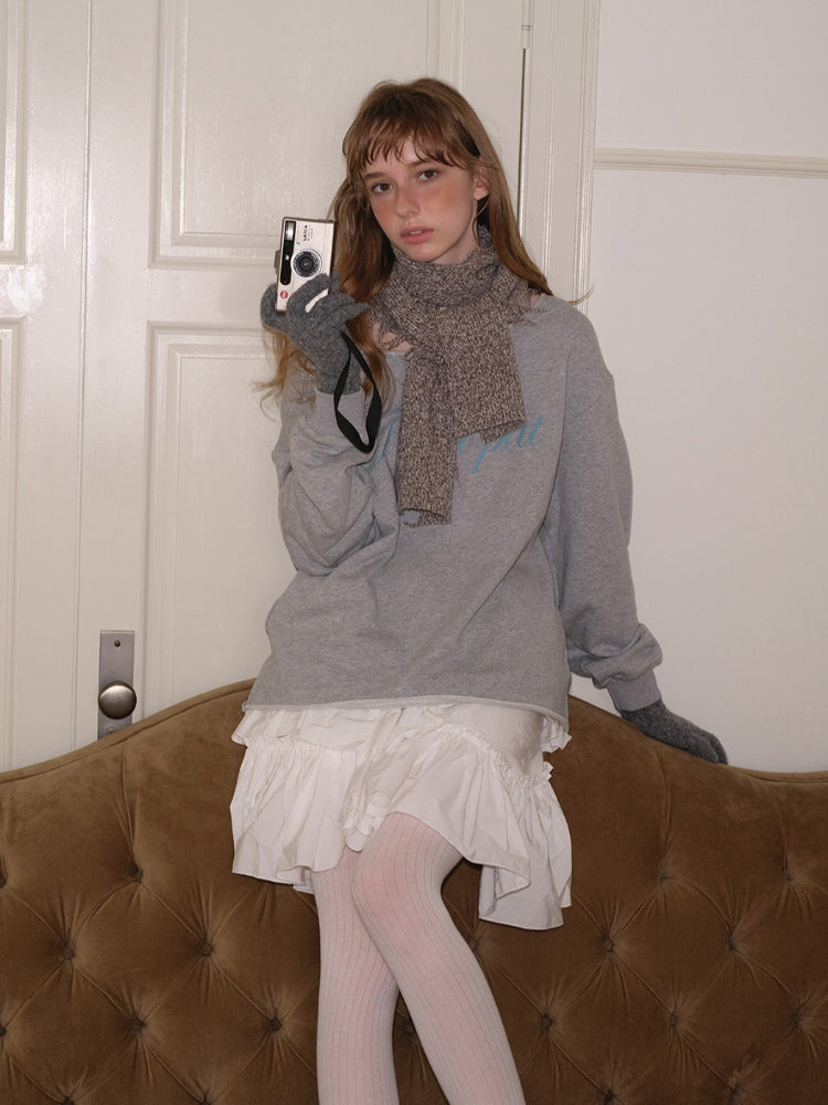 Model wearing a grey graphic sweatshirt, grey scarf, grey gloves, and a white ruffled skirt.