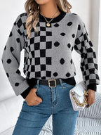 Woman wearing a grey knit sweater with a black checkerboard and polka dot pattern, paired with blue jeans and a white handbag.