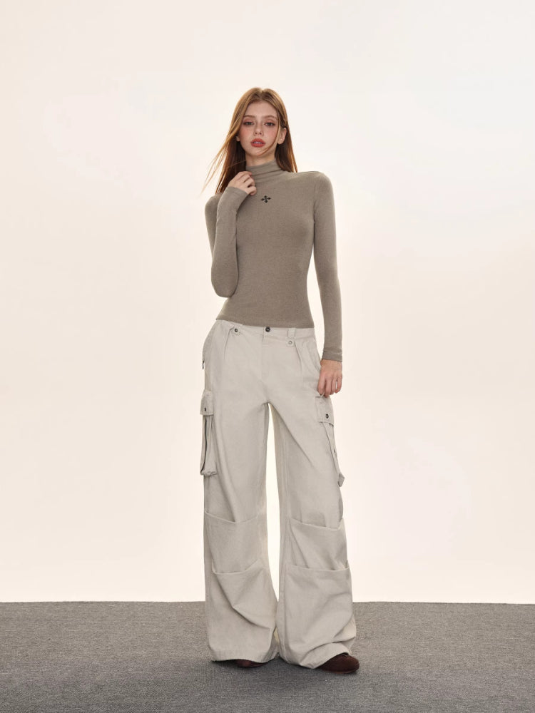 Full-body shot of a woman wearing a taupe turtleneck top and light beige wide-leg cargo pants.