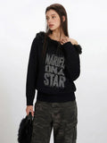 Close-up of a woman wearing a black off-the-shoulder knit sweater with faux fur detailing and a distressed graphic print.