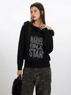 Close-up of a woman wearing a black off-the-shoulder knit sweater with faux fur detailing and a distressed graphic print.