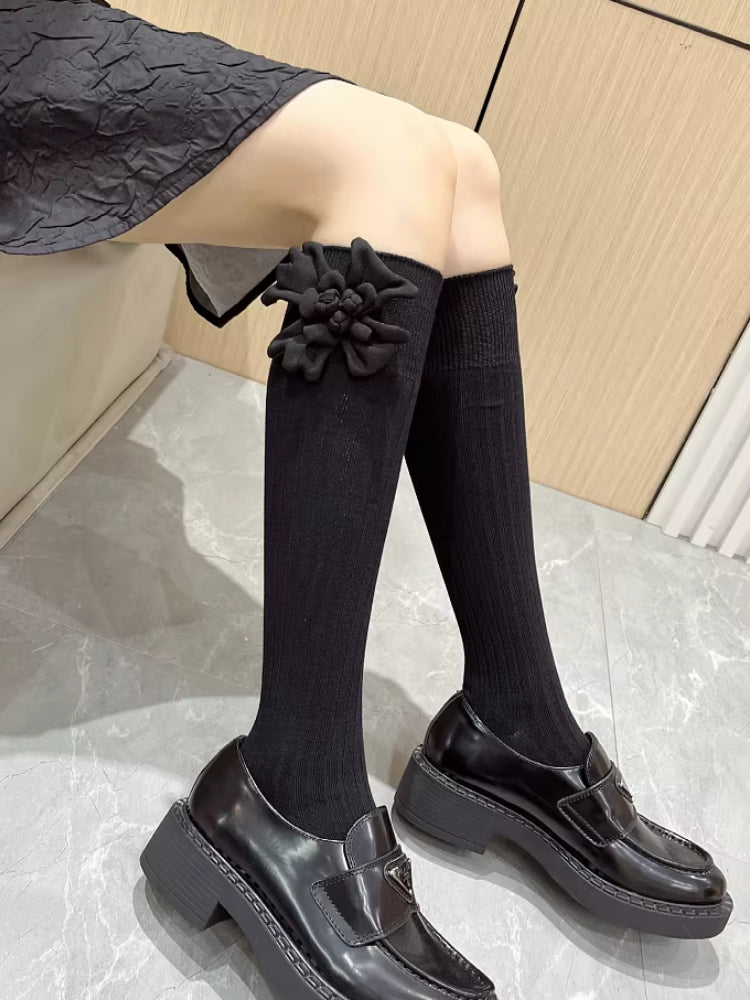 black knee-high socks with ribbed texture and a black flower applique on the cuff