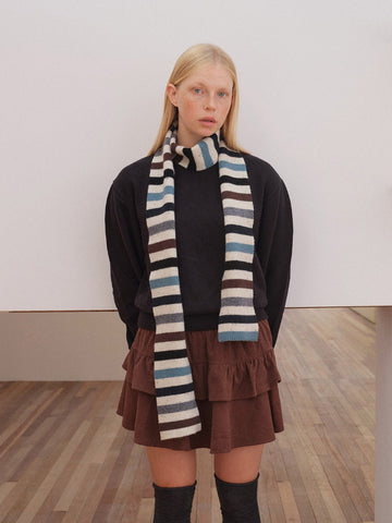 Woman wearing a striped knitted scarf with black, white, blue, and brown horizontal stripes