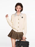 Woman wearing a cream-colored knit cardigan with a collared neckline and button-up front, paired with a brown pleated skirt.