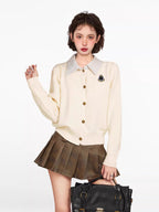 Woman wearing a cream-colored knit cardigan with a collared neckline and button-up front, paired with a brown pleated skirt.