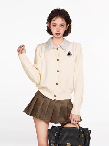Woman wearing a cream-colored knit cardigan with a collared neckline and button-up front, paired with a brown pleated skirt.