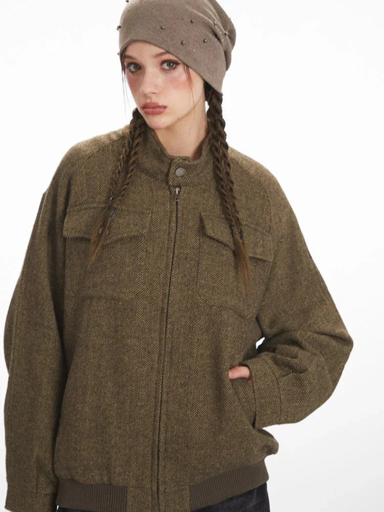 Close-up of the front of a brown herringbone bomber jacket with a stand collar and zipper.