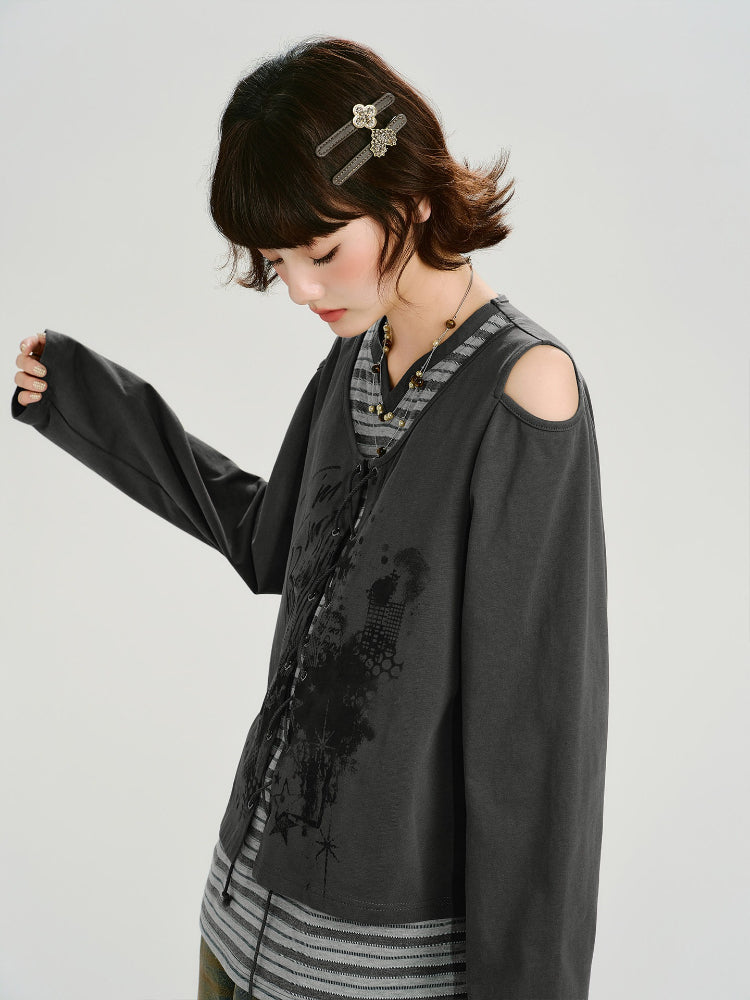 Woman wearing a dark gray graphic print cropped long-sleeve top with cold shoulder cutouts and a lace-up front over a gray and white striped t-shirt.