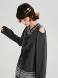 Woman looking down while wearing a dark gray graphic print cropped long-sleeve top with cold shoulder cutouts and a lace-up front over a gray and white striped t-shirt.