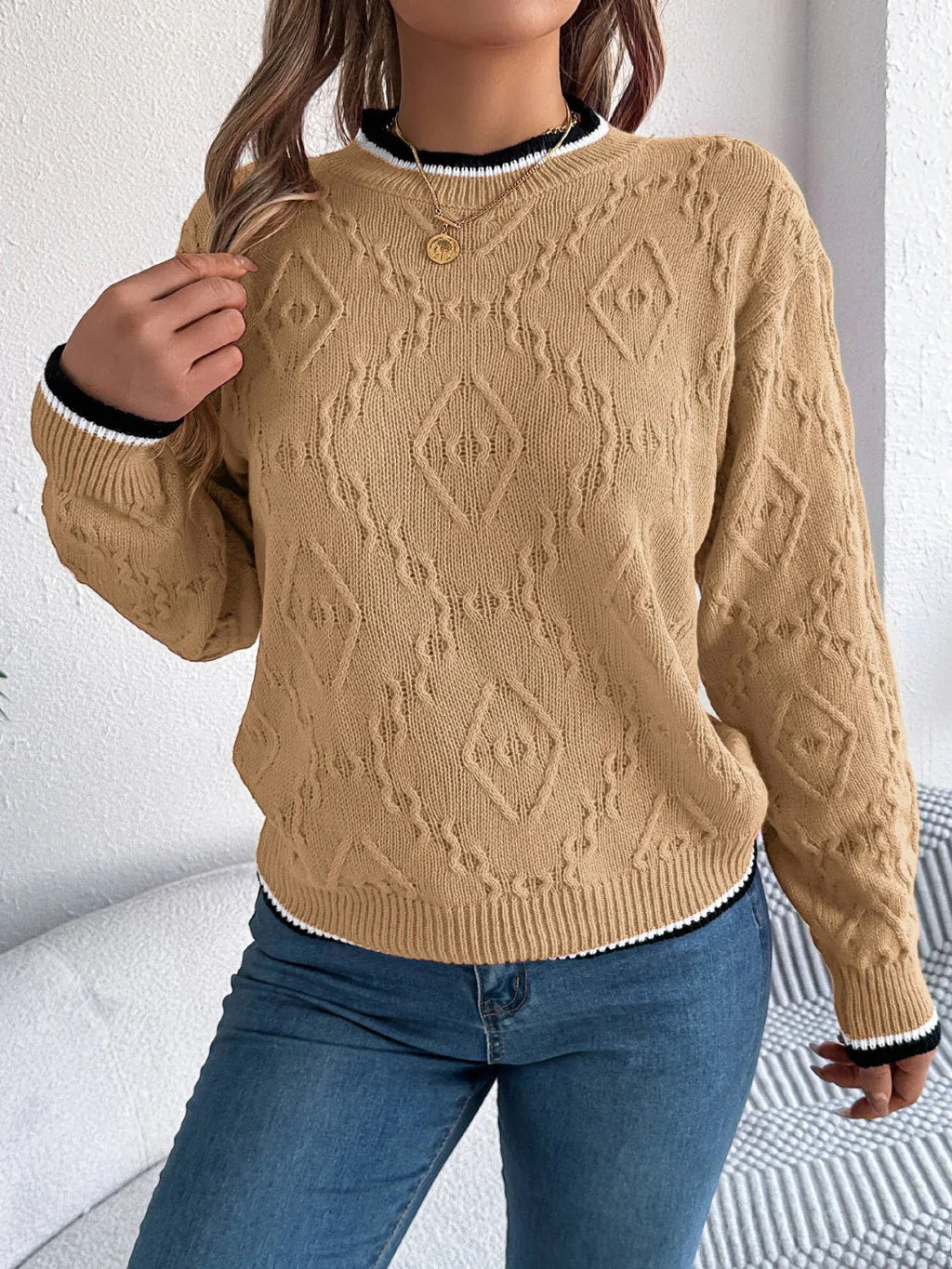 Woman with her hand in her hair, wearing a tan cable knit sweater with a diamond pattern.