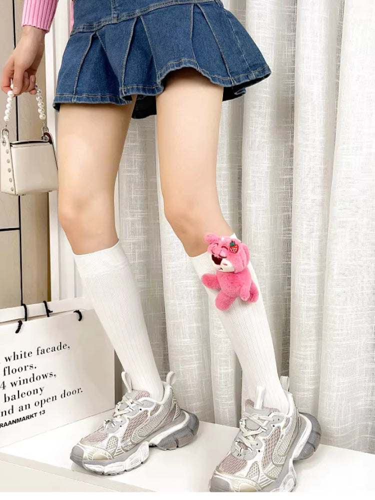 Person wearing white knee-high socks with a pink plush bear charm and a denim skirt.