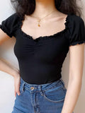 Woman wearing a black ribbed knit top with off-the-shoulder design and ruched front