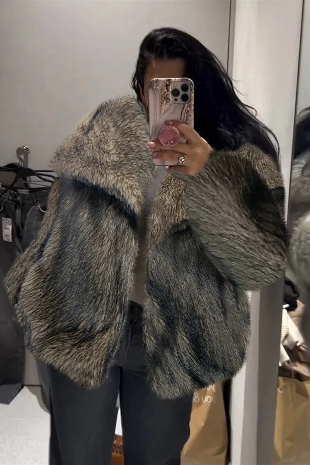 Woman taking a mirror selfie in a grey faux fur jacket.