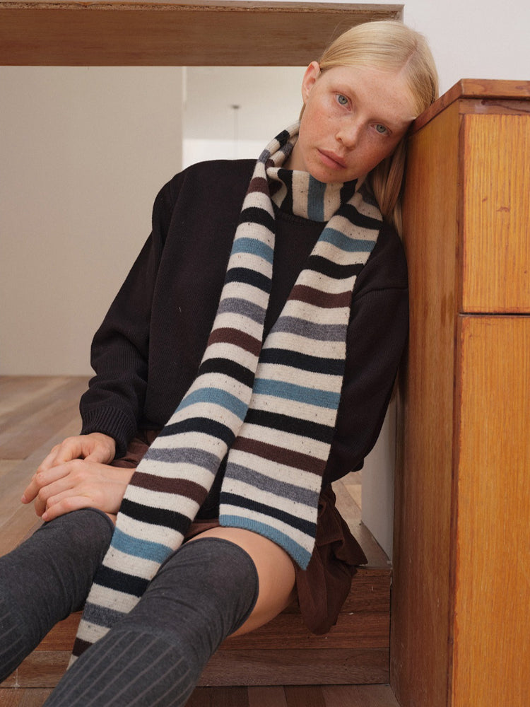 Woman leaning against wooden furniture with striped scarf
