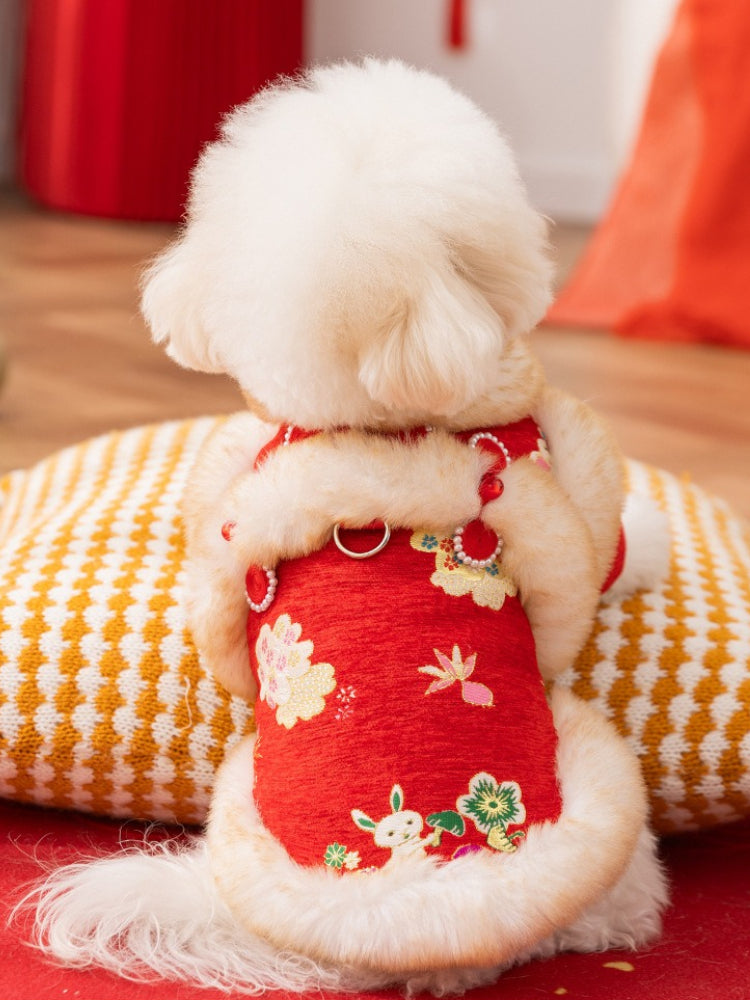 Rear view of a small white dog in a red coat with faux fur trim, showing embroidered floral patterns and a D-ring for leash attachment.