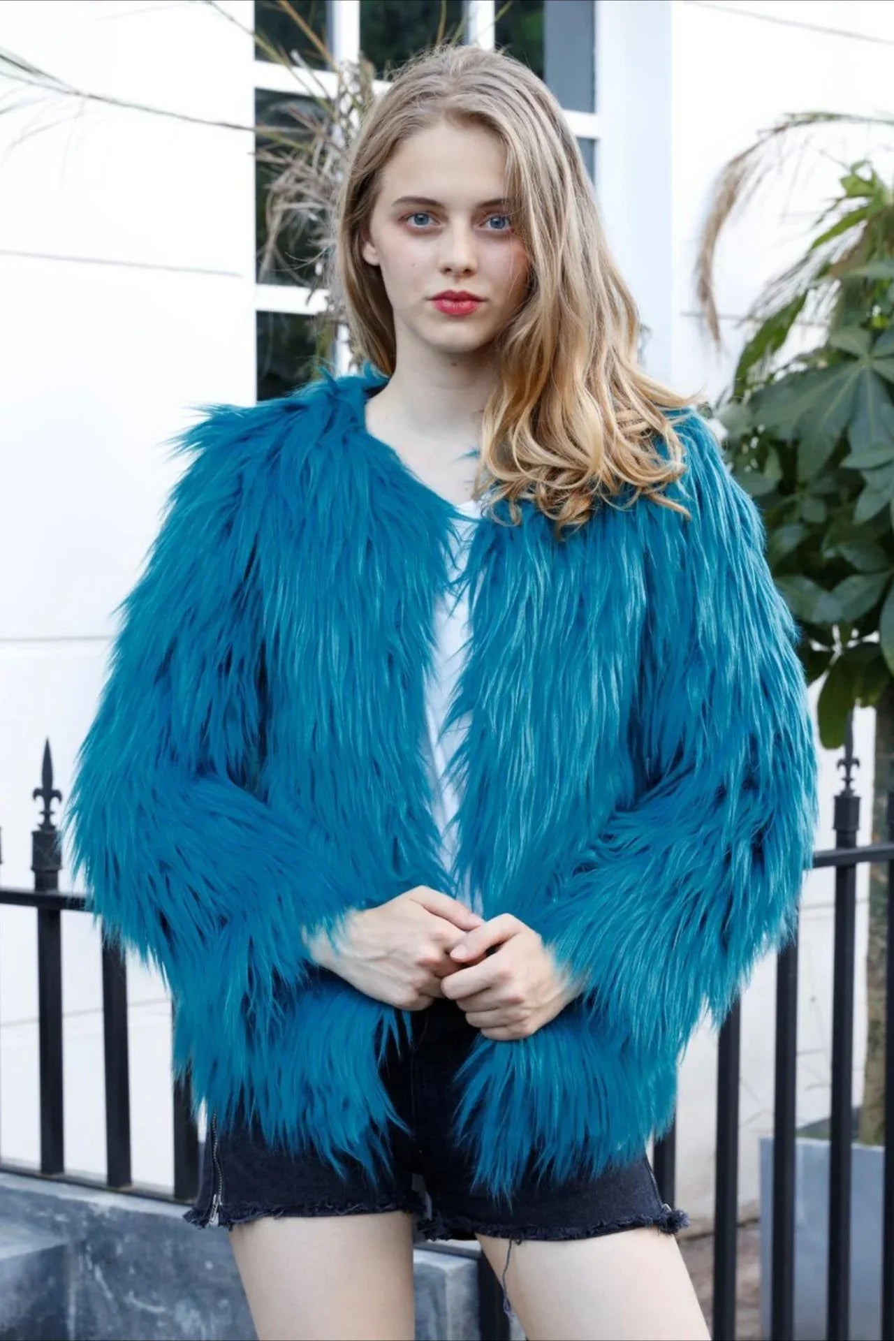 Woman wearing a teal faux fur jacket with a white t-shirt and black shorts Main image