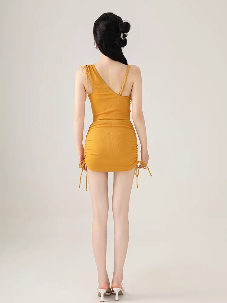 Back view of a woman wearing a yellow one-shoulder ribbed knit bodysuit with adjustable drawstring details