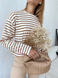 Woman wearing a white and brown striped long sleeve top and beige pants, holding a bouquet of dried flowers and a woven handbag.
