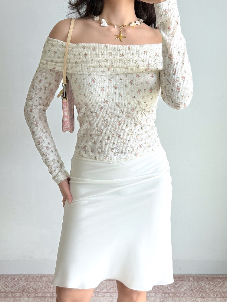 Woman wearing a white off-the-shoulder top with a floral print and long sleeves.