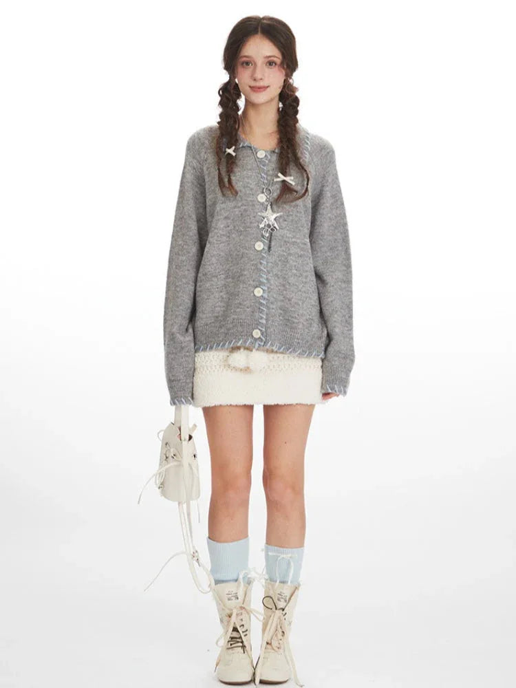 Model wearing a grey knitted cardigan with white buttons and blue contrast trim