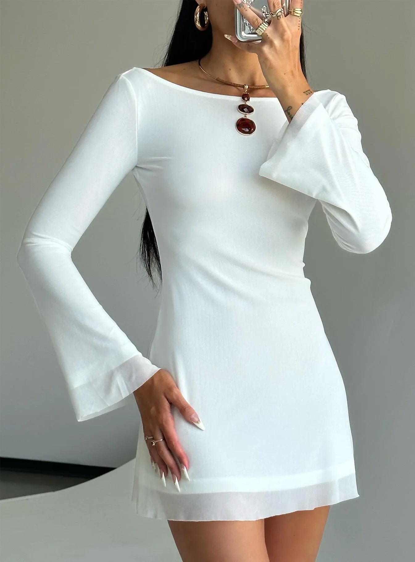 Woman in a white long-sleeve mini dress with bell sleeves and sheer hem Main image
