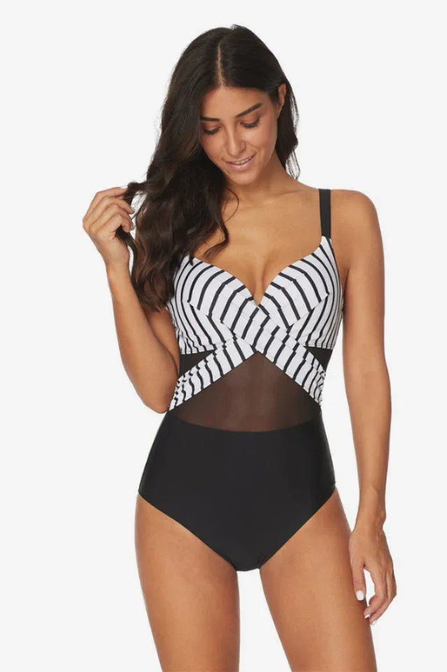 Woman adjusting her hair while wearing a black and white striped one-piece swimsuit with mesh accents