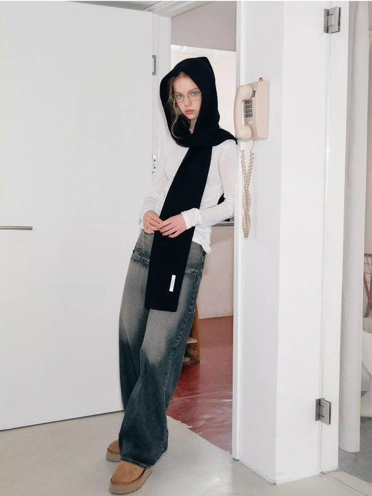 Woman leaning against a doorway wearing a black knit hooded scarf and jeans