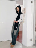 Woman leaning against a doorway wearing a black knit hooded scarf and jeans