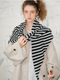 Woman wearing a black and white striped scarf draped around her neck and over a beige coat.