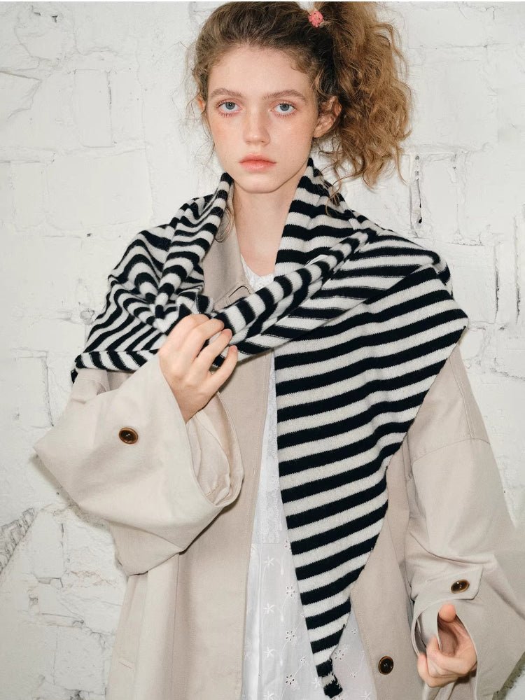 Woman wearing a black and white striped scarf draped around her neck and over a beige coat.
