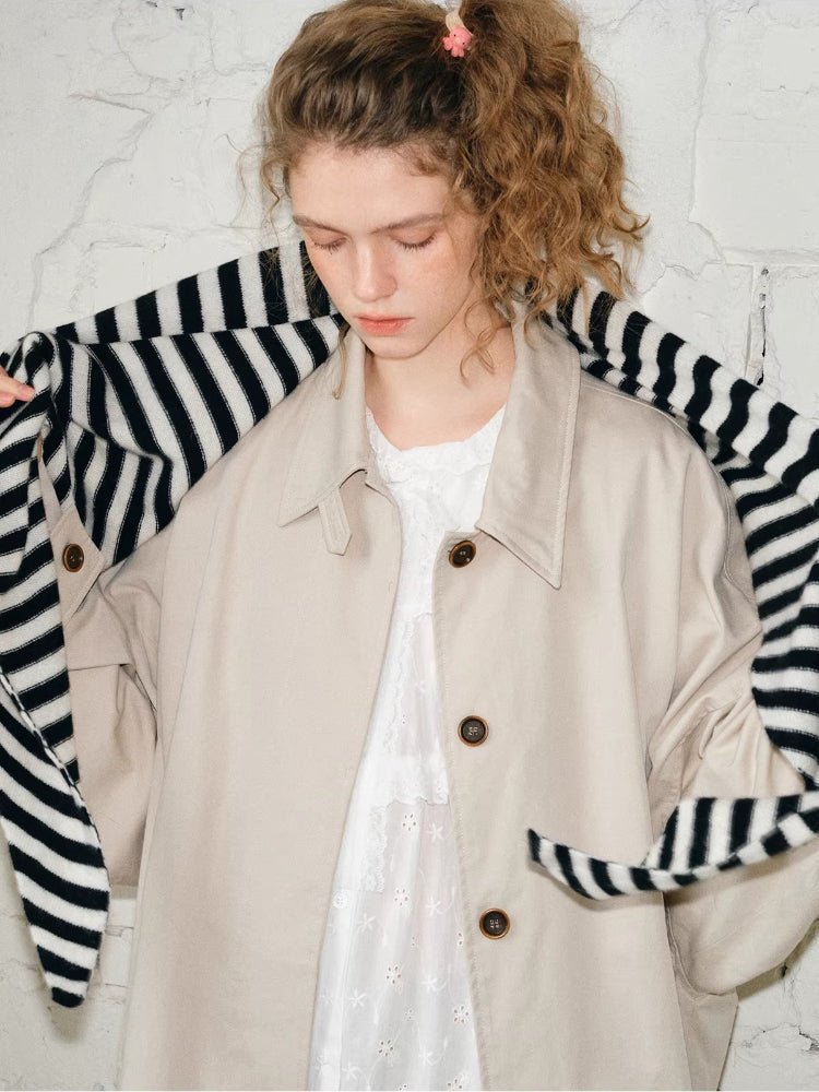 Woman wearing a black and white striped scarf draped around her neck and over a beige coat.