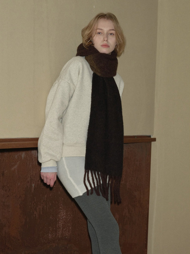 Woman in a light grey sweatshirt and dark brown scarf standing with hands on hips.