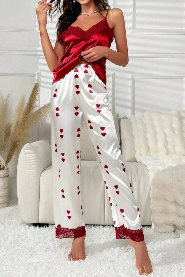 Woman wearing a red satin camisole with lace trim and white satin wide leg pajama pants with a red heart print. Main image