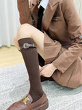 Woman wearing brown knee-high socks with a buckle strap and brown loafers, dressed in a brown blazer and skirt.