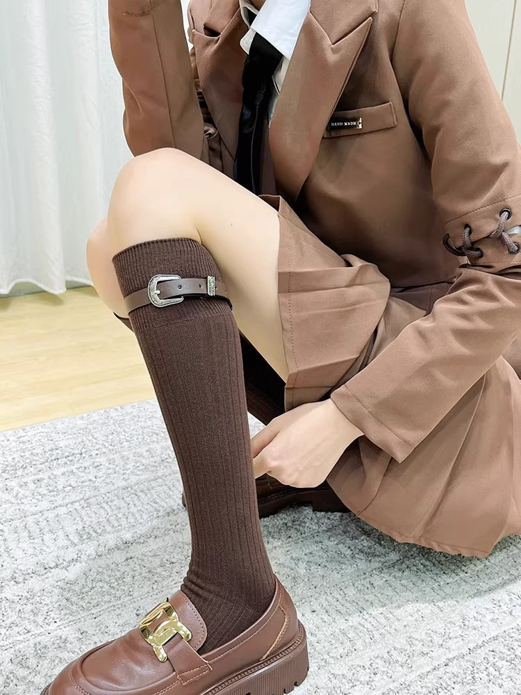 Woman wearing brown knee-high socks with a buckle strap and brown loafers, dressed in a brown blazer and skirt.