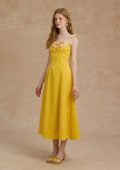 A woman in a yellow floral dress and straw hat standing outdoors