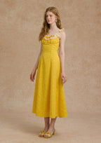 A woman in a yellow floral dress and straw hat standing outdoors