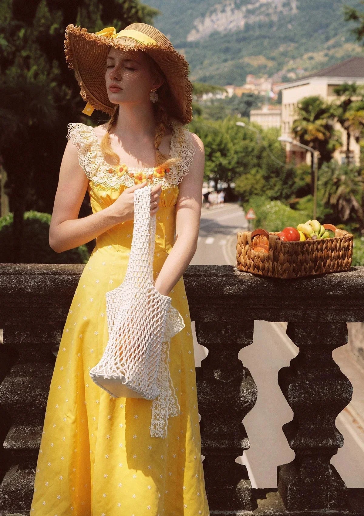 Woman wearing a yellow floral maxi dress, straw hat, and holding a white net bag