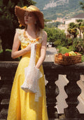 Woman wearing a yellow floral maxi dress, straw hat, and holding a white net bag