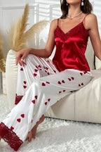 Woman sitting on a couch wearing a red satin camisole with lace trim and white satin pajama pants with a red heart print.