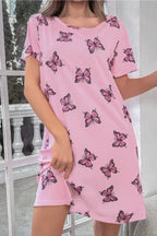 Woman wearing a pink short-sleeve nightgown with a scattered pink butterfly print, standing indoors.