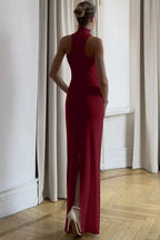 Back view of a woman in a burgundy halter maxi dress with a leg slit.