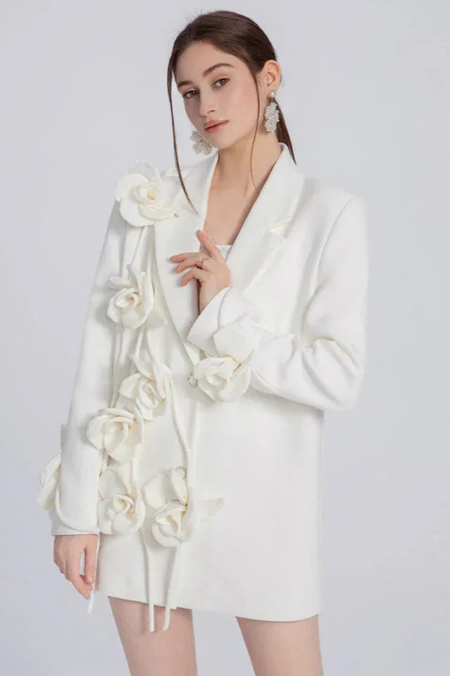 Woman wearing a white blazer with floral appliqués on the left shoulder and down the front.