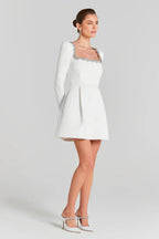Side view of a woman in a white formal dress with a pleated skirt and long sleeves